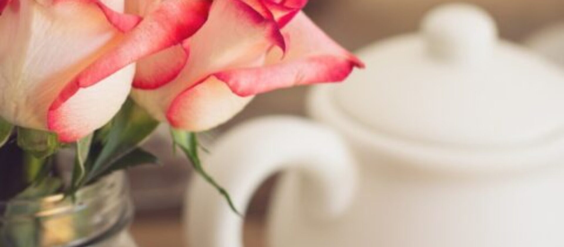 A bouquet of red tipped white rose in a glass jar next to a white tea pot